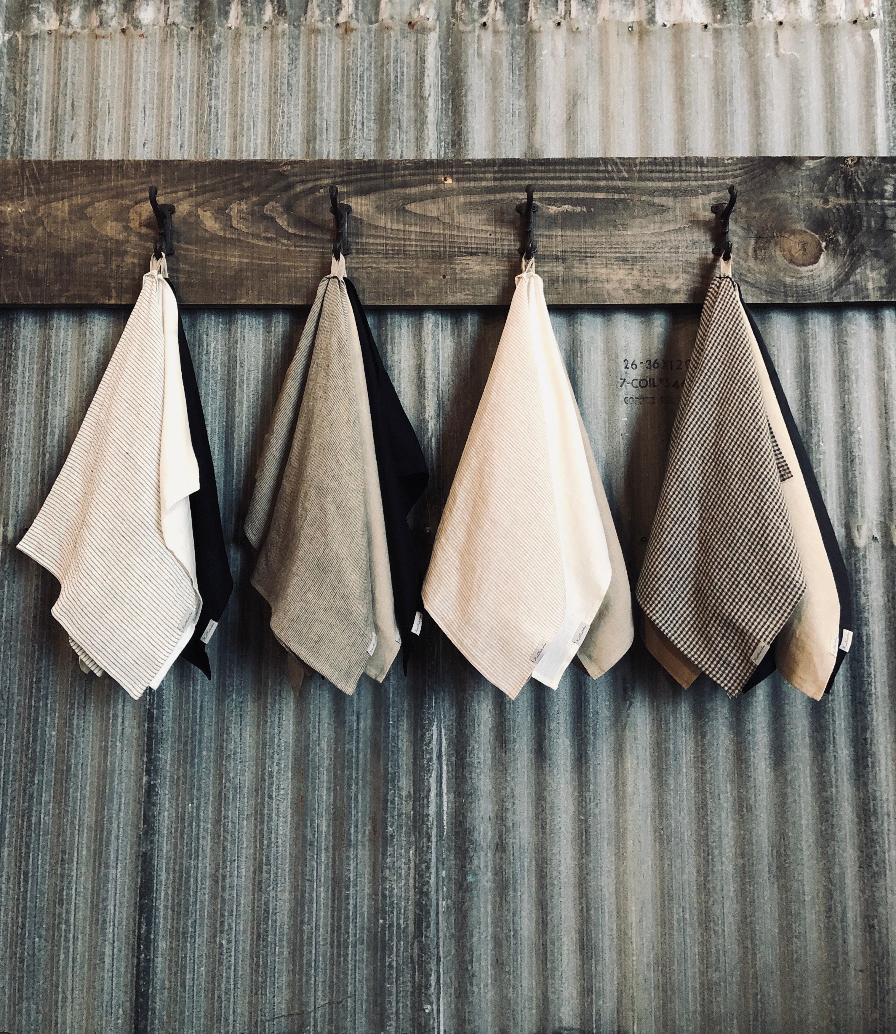 Multiple striped, checked, and plain tea towels hanging on hooks mounted on tin wall