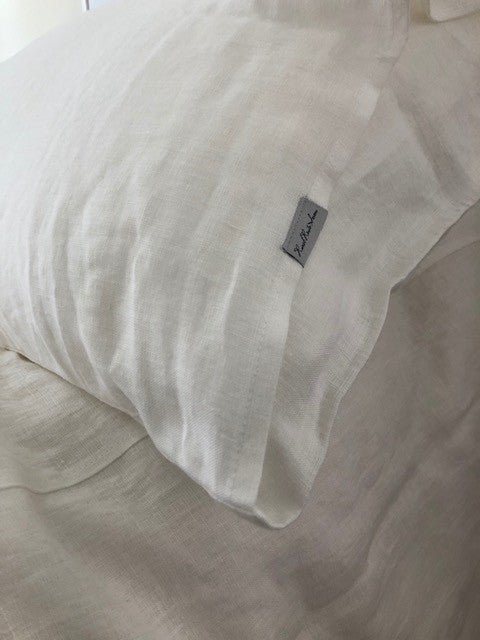 Close up of fluffly white pillow with white flax linen Oeko-Tex Certified Organic European linen pillowcase resting on Oeko-Tex Certified Organic European linen duvet cover on perfectly made bed