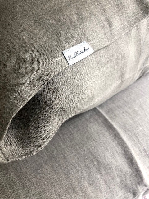 Close up of fluffy pillow with Oeko-Tex Certified Organic European Linen natural flax linen pillowcase and Rural Route Seven logo brand label resting on Oeko-Tex Certified Organic European Linen natural flax linen duvet cover on bed with sunlight streaming in