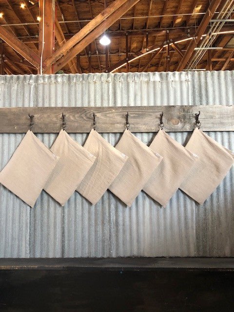 Six Natural Linen & Wool Dish Drying Mats hanging on hooks against tin wall