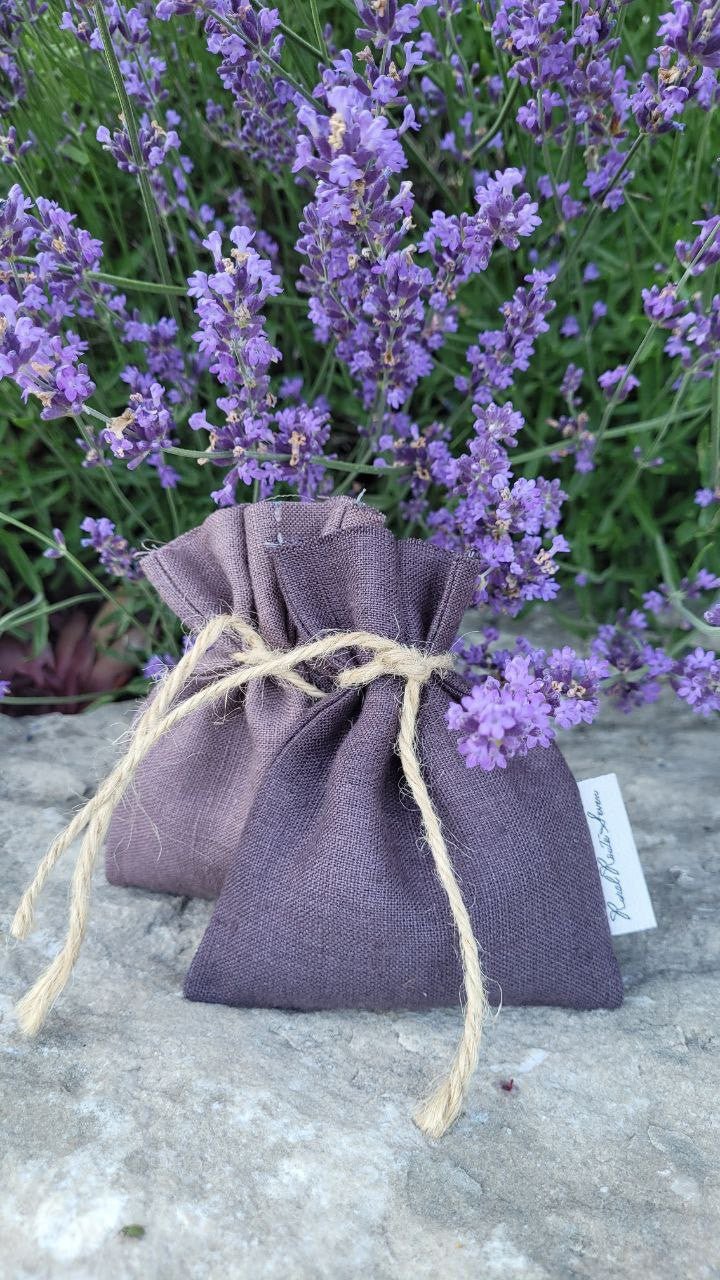 Linen Lavender Sachets in dark and light purple linen, tied with twine resting on stone in lavender garden