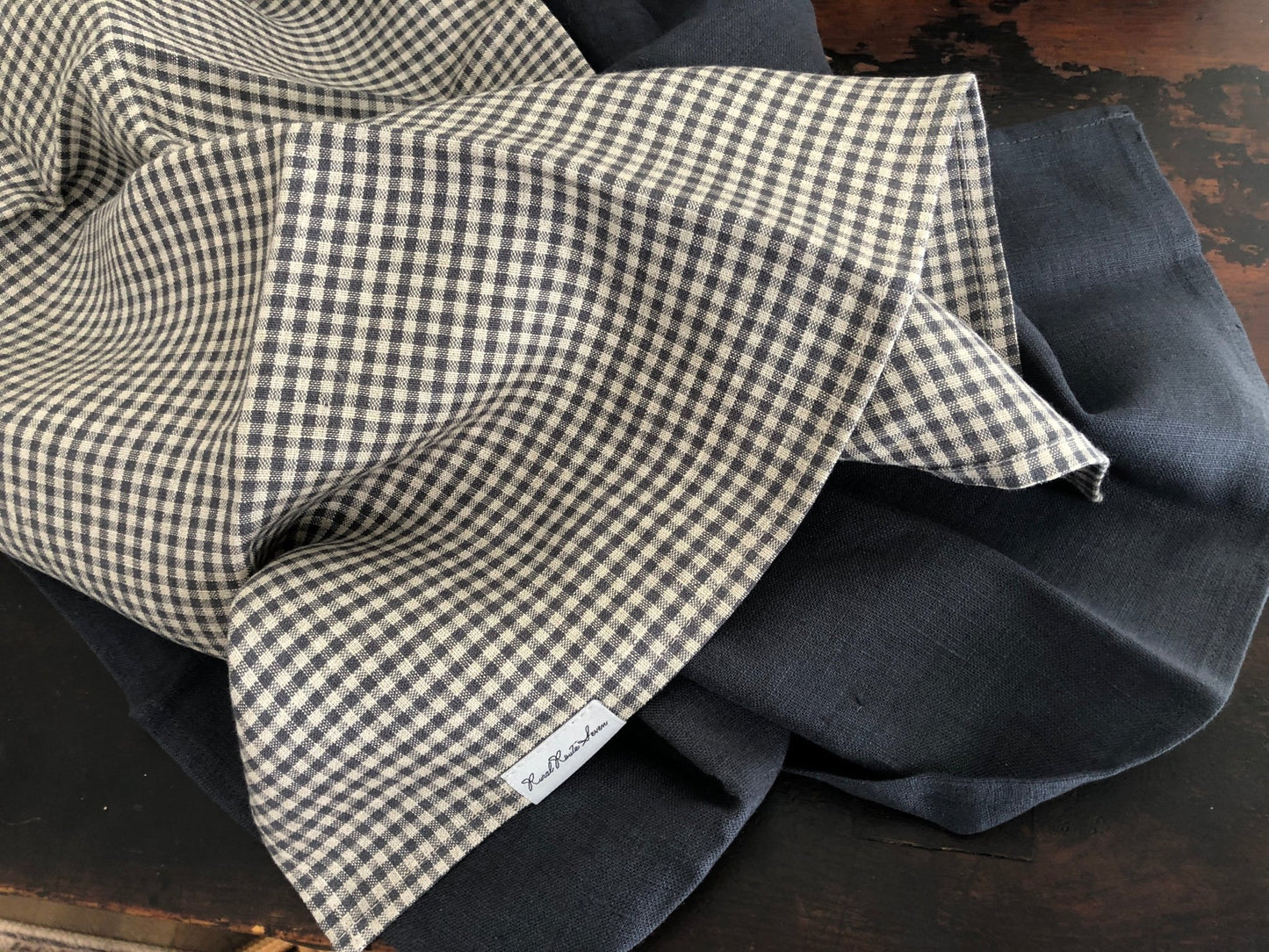 Small charcoal grey and natural flax checked linen tea towel and charcoal grey linen tea towel on distressed black cupboard