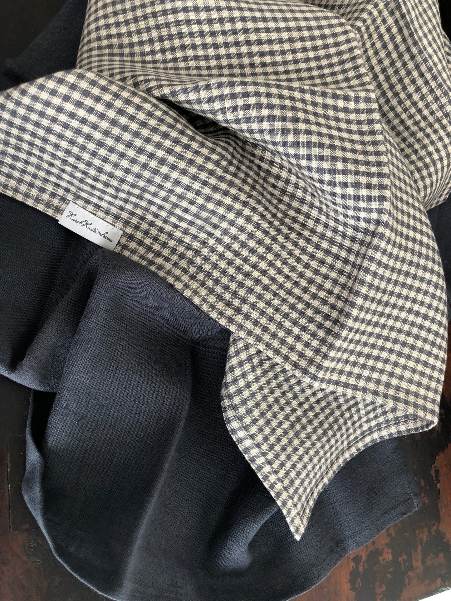 Small charcoal grey and natural flax checked linen tea towel and charcoal grey linen tea towel on distressed black cupboard