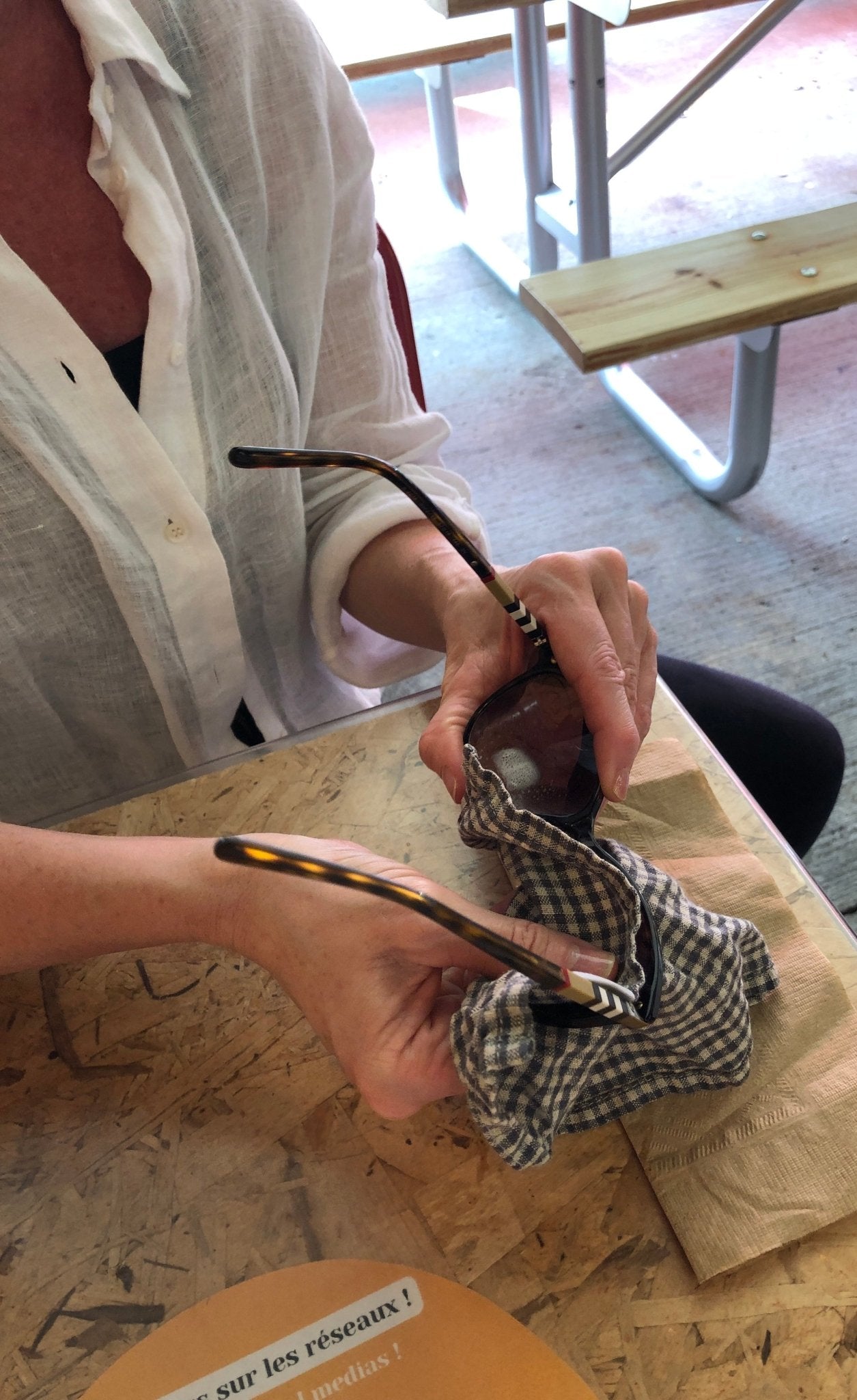Torso of women wearing white linen blouse sitting at table cleaning sunglasses with Linen Handkerchief from Rural Route Seven