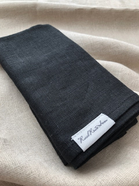 Close up of folded black stonewashed European linen tea towel resting on stonewashed natural flax linen tablecloth