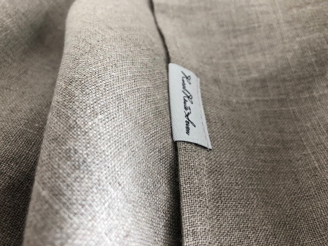 Close up of textured stonewashed European linen tablecloth in natural flax linen with Rural Route Seven logo brand label with light grey background and black font print