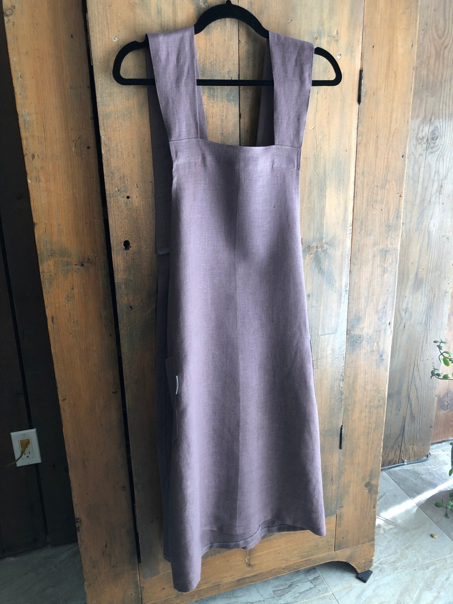 Lavender coloured linen Japanese cross back pinafore apron hanging on an antique pine cupboard door