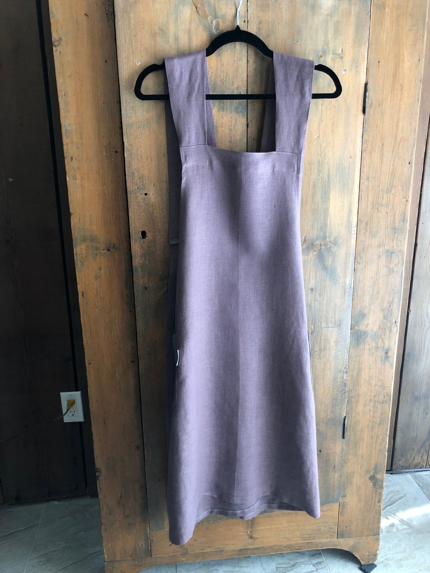 Lavender coloured linen Japanese cross back pinafore apron hanging on an antique pine cupboard door