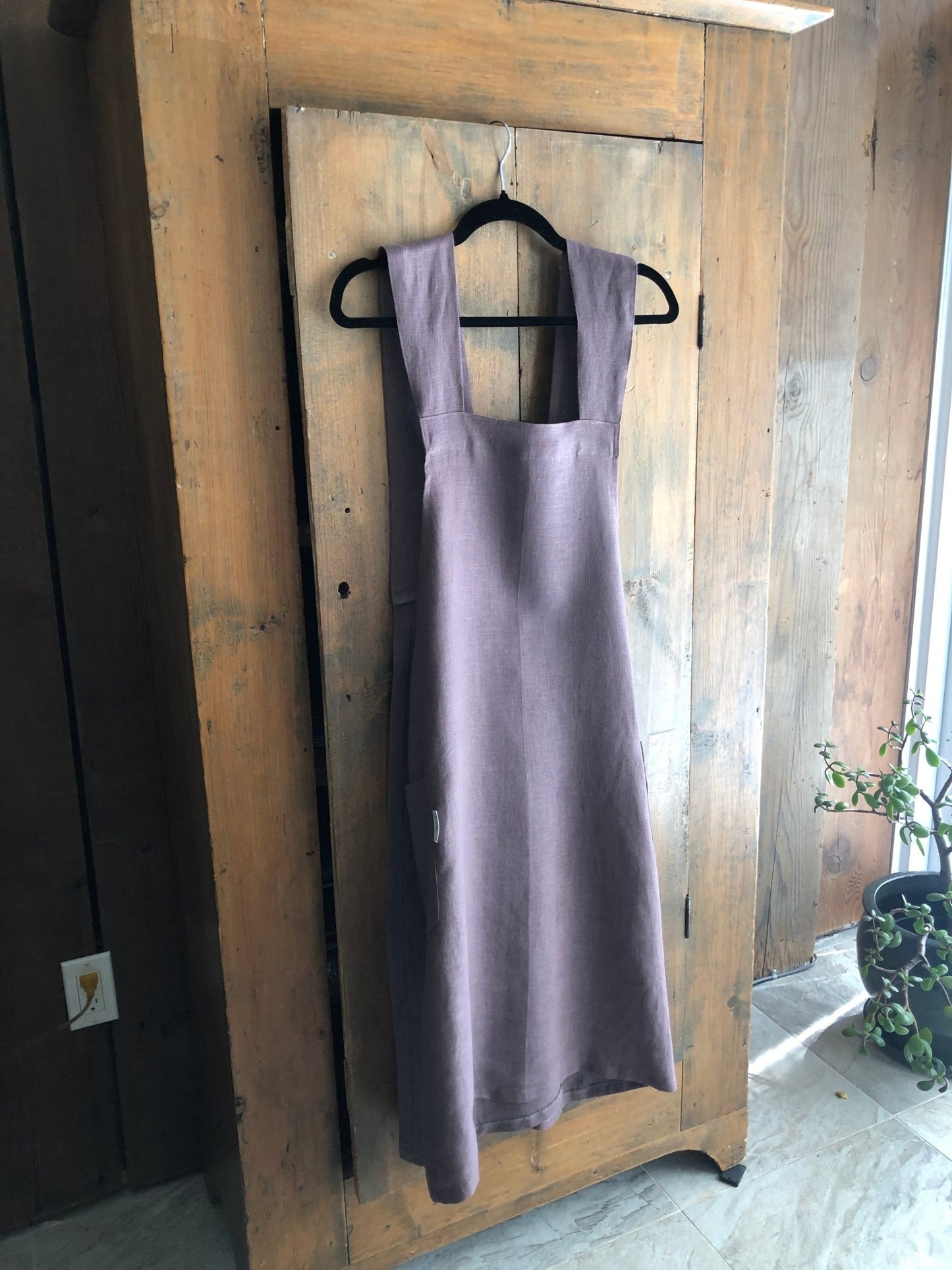 Lavender coloured linen Japanese cross back pinafore apron hanging on an antique pine cupboard door