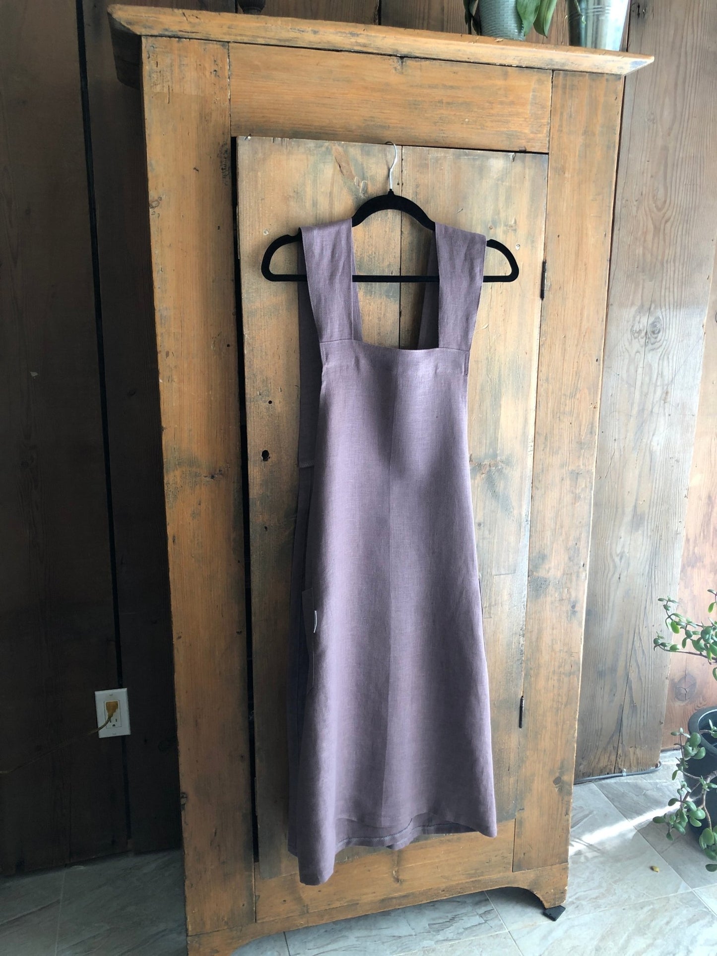 Lavender coloured linen Japanese cross back pinafore apron hanging on an antique pine cupboard door