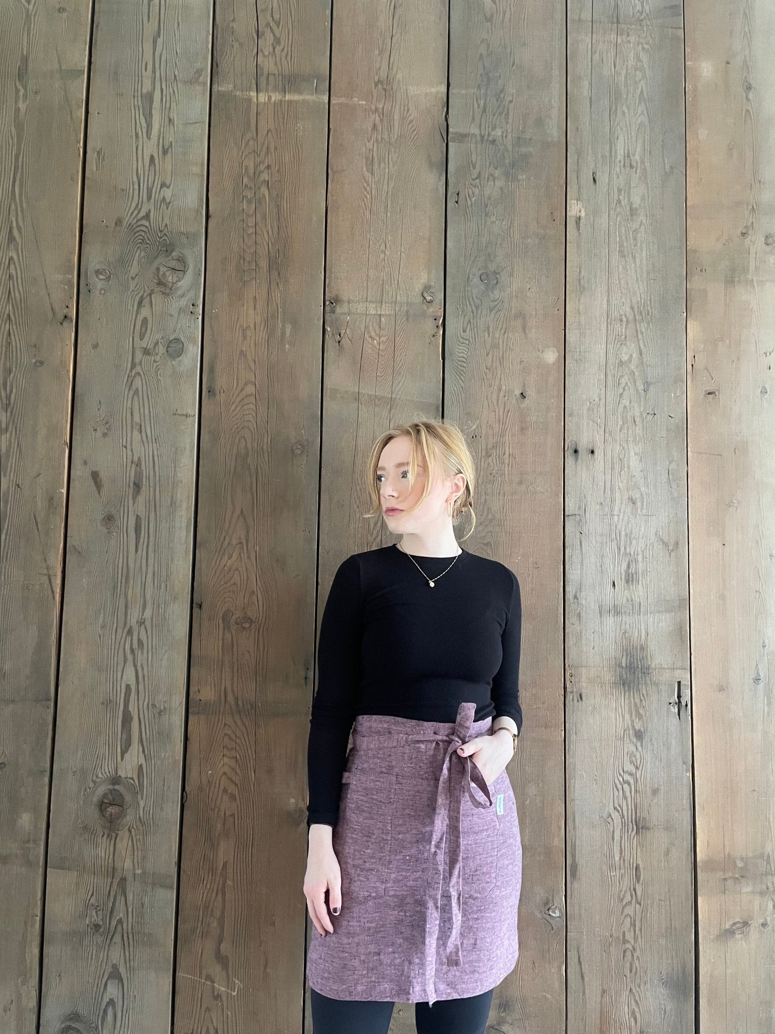 Young woman wearing linen half apron in pink black melange, hand in pocket