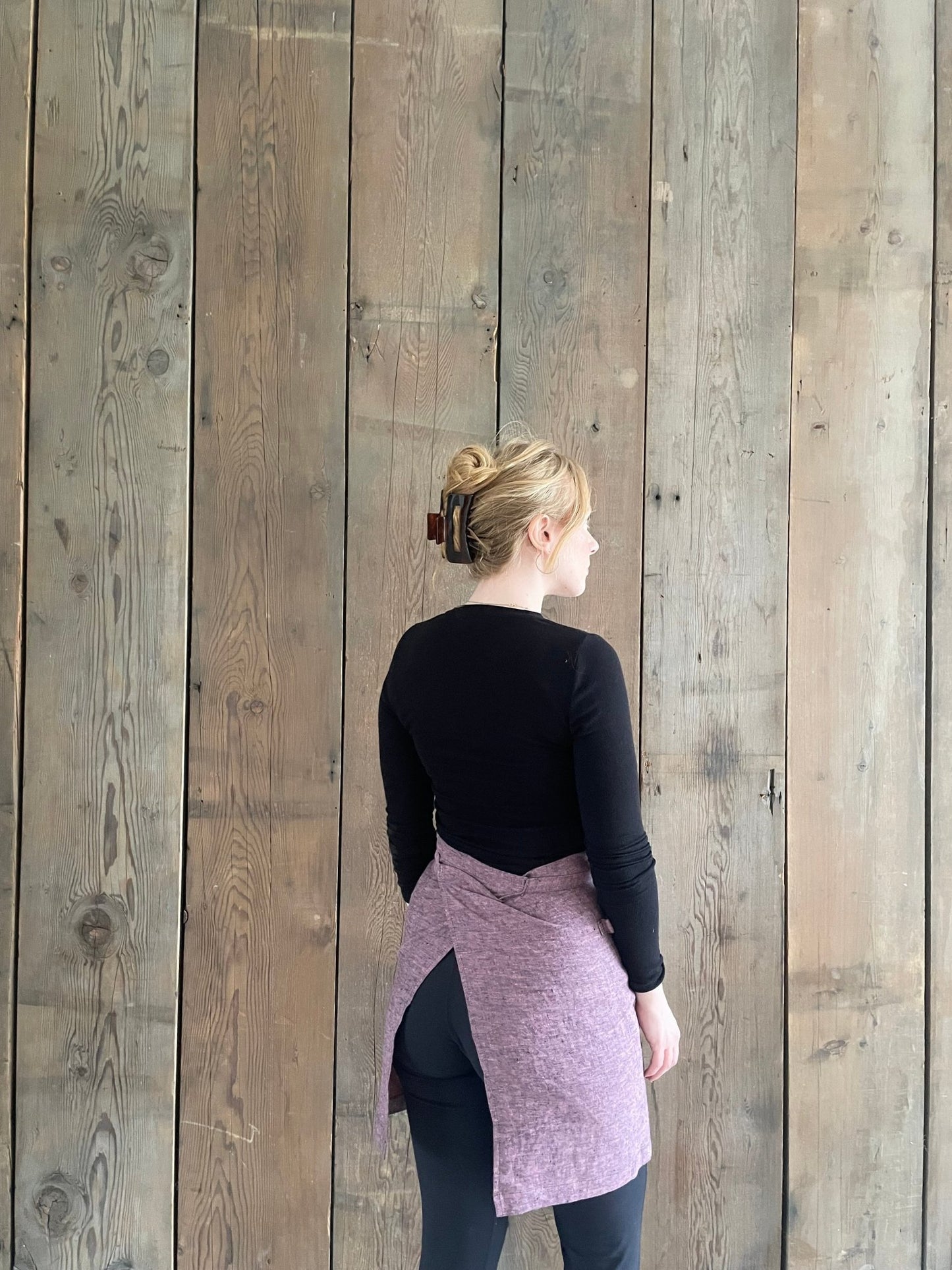 Rear view of young woman wearing linen half apron in pink black melange 