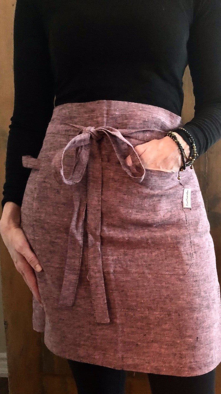 Close up of woman wearing linen half apron in pink black melange with hand in pocket