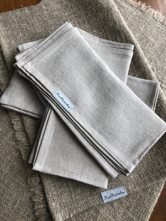 Folded asymmetrical stack of natural Linen Napkins, Set of 6, with Rural Route Seven label resting on table