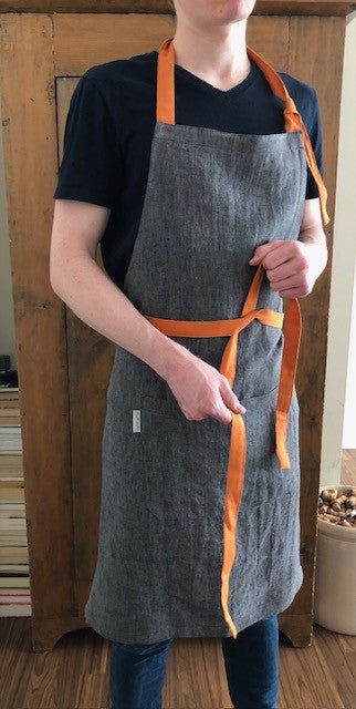 Man wearing navy t-shirt and grey black melange Men's Linen Apron with pumpkin orange canvas ties, Rural Route Seven.