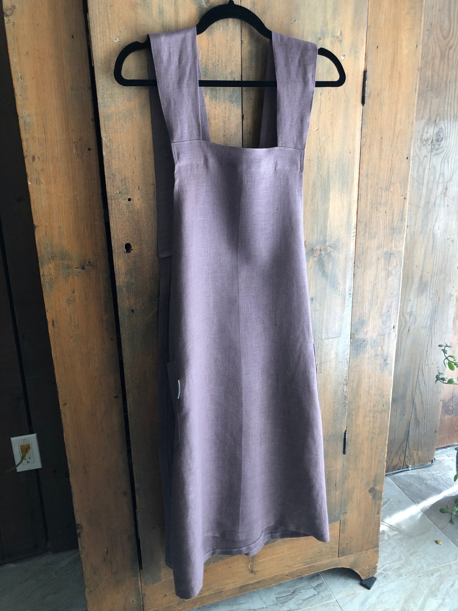 Lavender coloured linen Japanese cross back pinafore apron hanging on an antique pine cupboard door