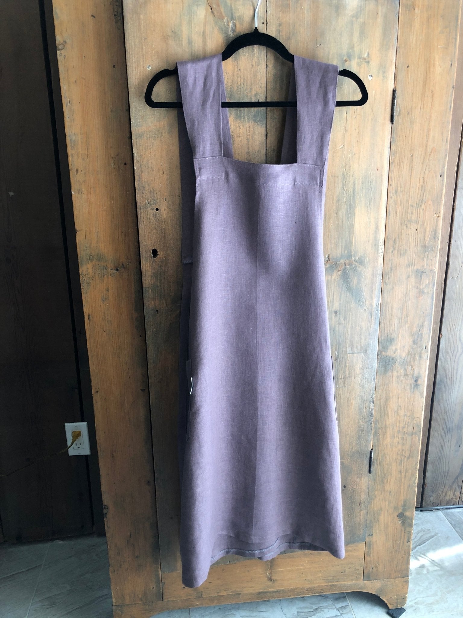 Lavender coloured linen Japanese cross back pinafore apron hanging on an antique pine cupboard door
