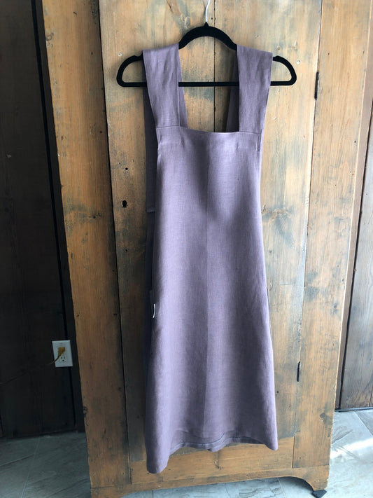 Lavender coloured linen Japanese cross back pinafore apron hanging on an antique pine cupboard door